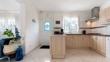 A modern kitchen with a central island, light wood cabinets, and a white tiled backsplash.