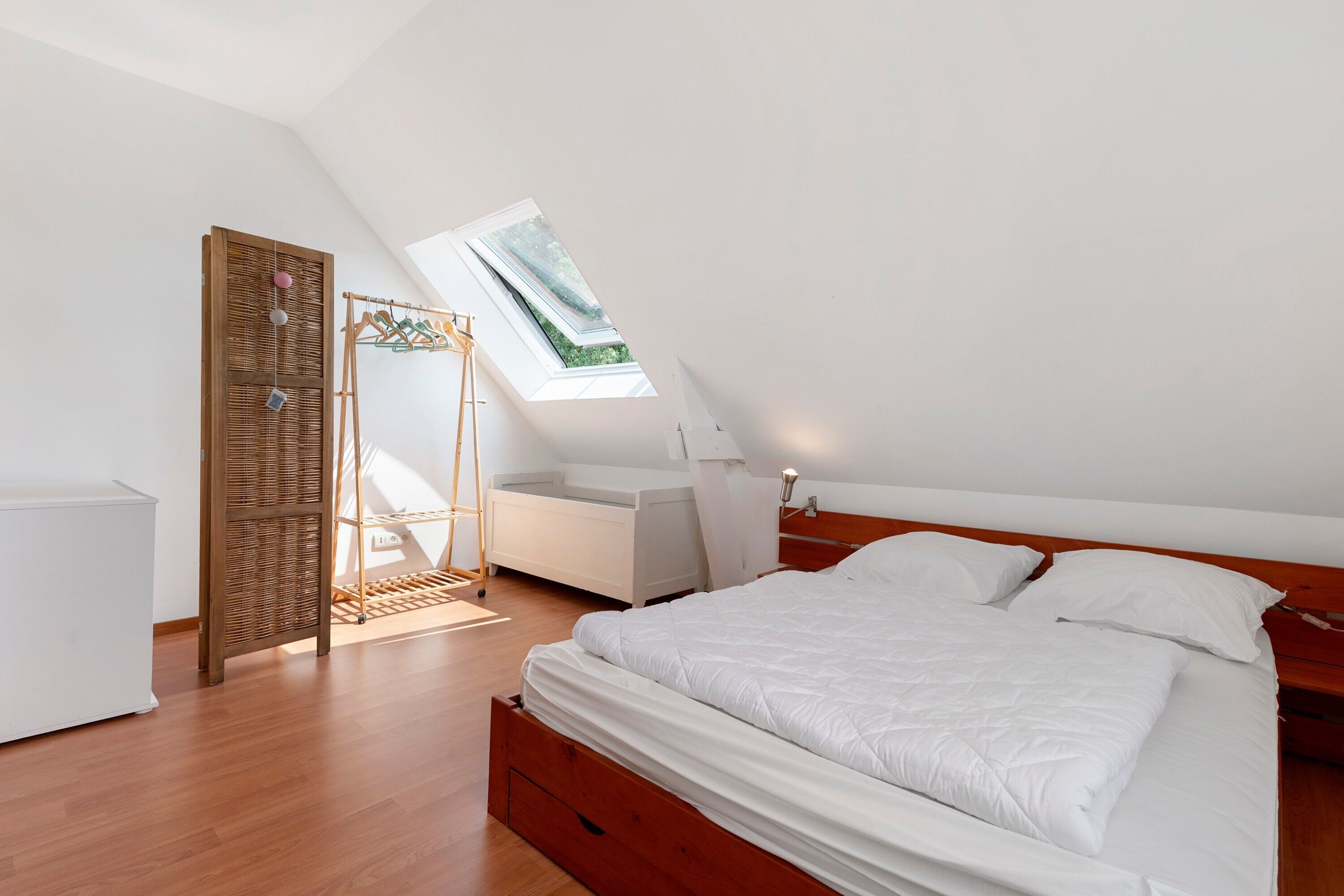 A bedroom with a skylight, a bed, a bedside table, a wardrobe, and a hanging rack.