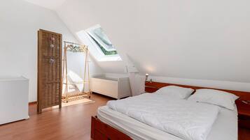 A bedroom with a skylight, a bed, a bedside table, a wardrobe, and a hanging rack.