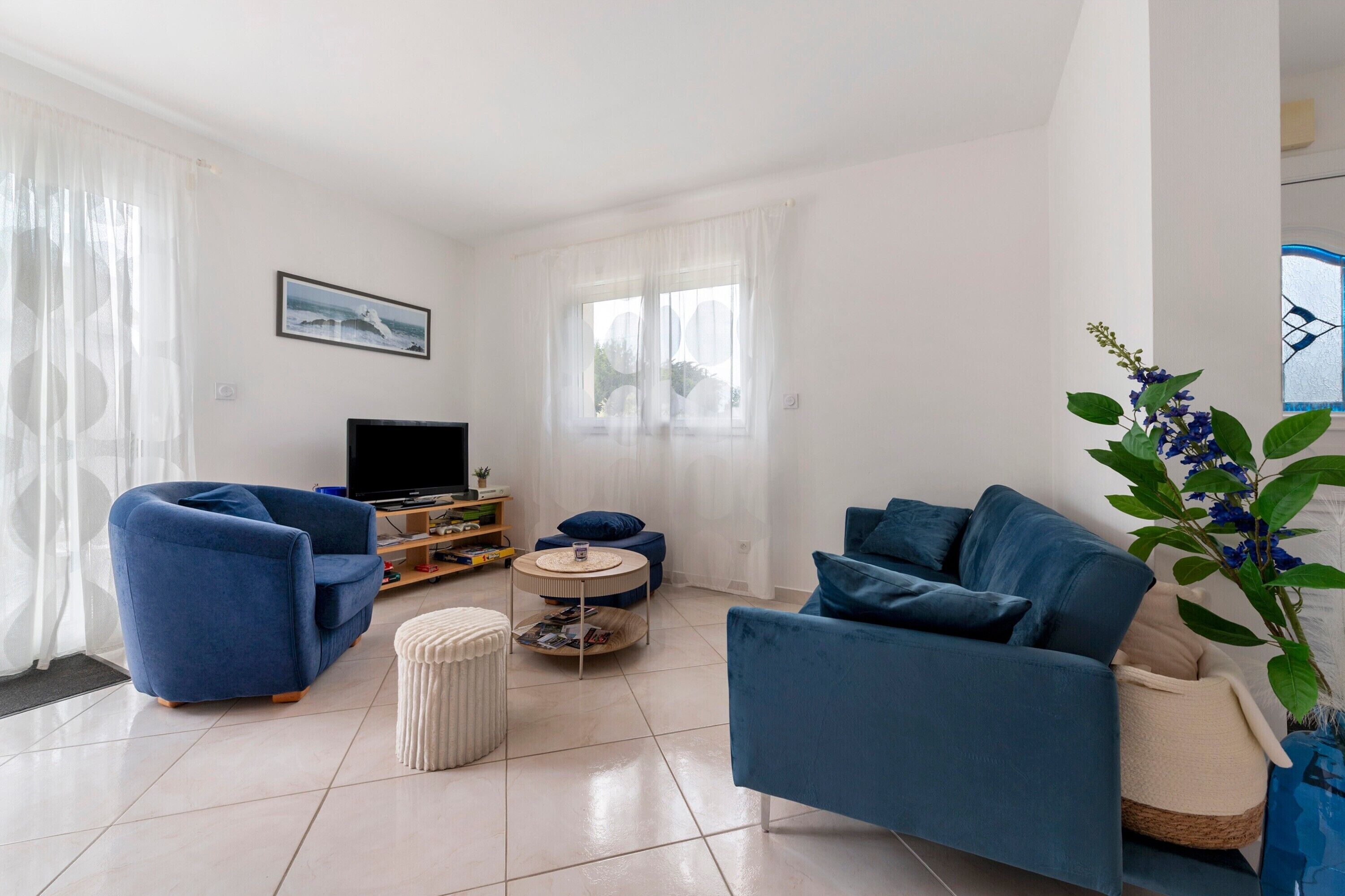 Una sala de estar con un sofá azul, un televisor, una mesita redonda y una planta.