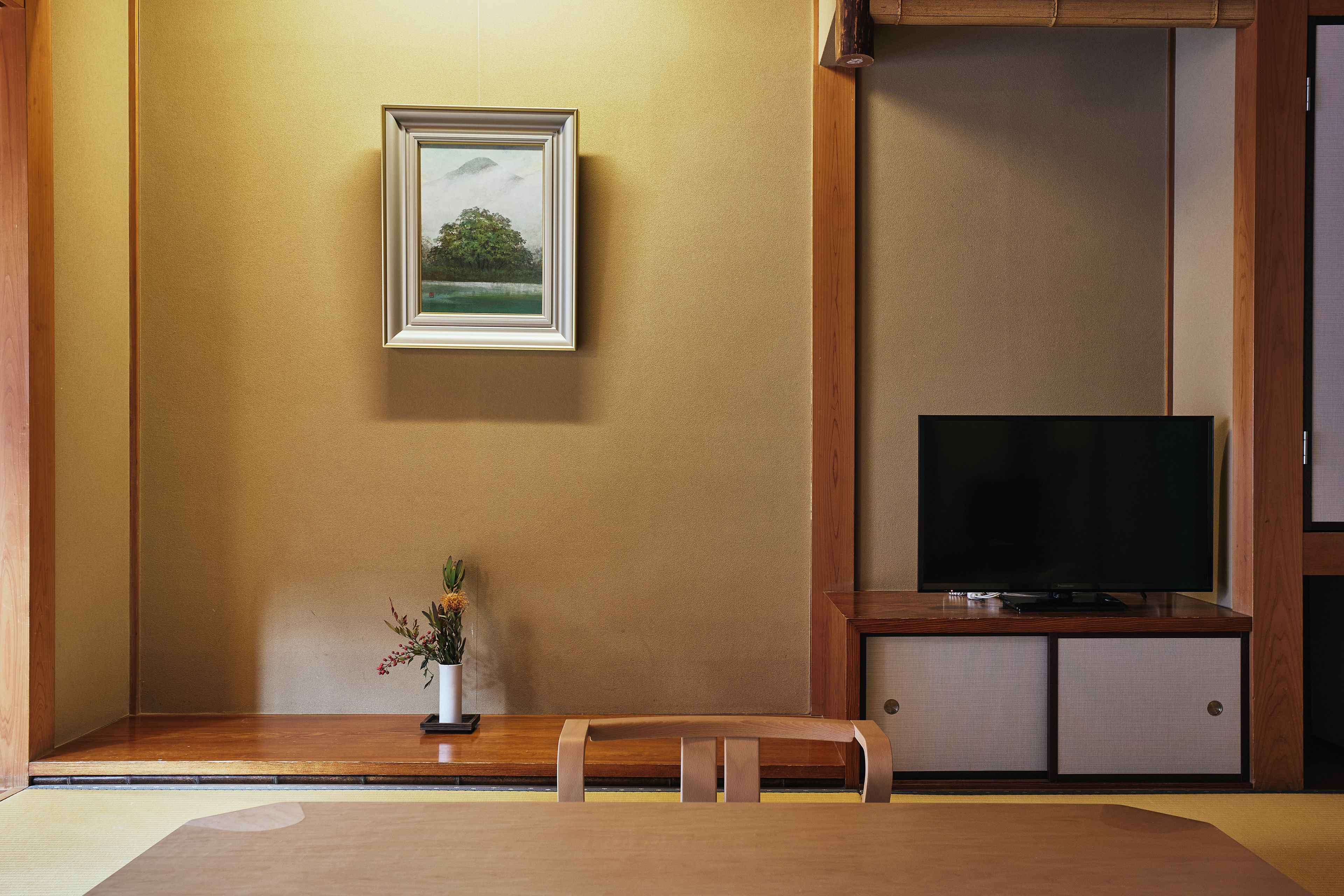 A room with a television on a wooden stand, a framed picture on the wall, and a small table with a plant.
