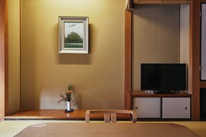 A room with a television on a wooden stand, a framed picture on the wall, and a small table with a plant.