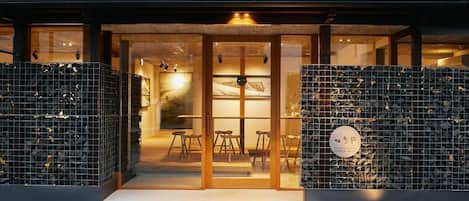 A building entrance with glass doors, a seating area inside, and a sign with Japanese characters.