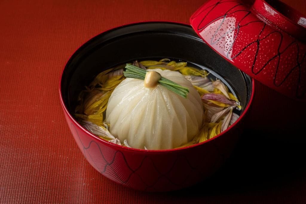 A bowl of soup with a dumpling and a garnish on a red table.
