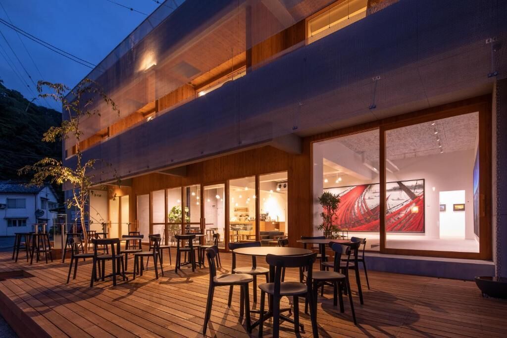 A modern building with a wooden deck, outdoor seating, and large windows.