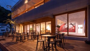 Een modern gebouw met een houten terras, buiten zitplaatsen en grote ramen.