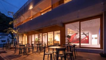 A modern building with a wooden deck, outdoor seating, and large windows.