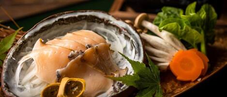 A dish with sliced fish on a plate, accompanied by vegetables and herbs.