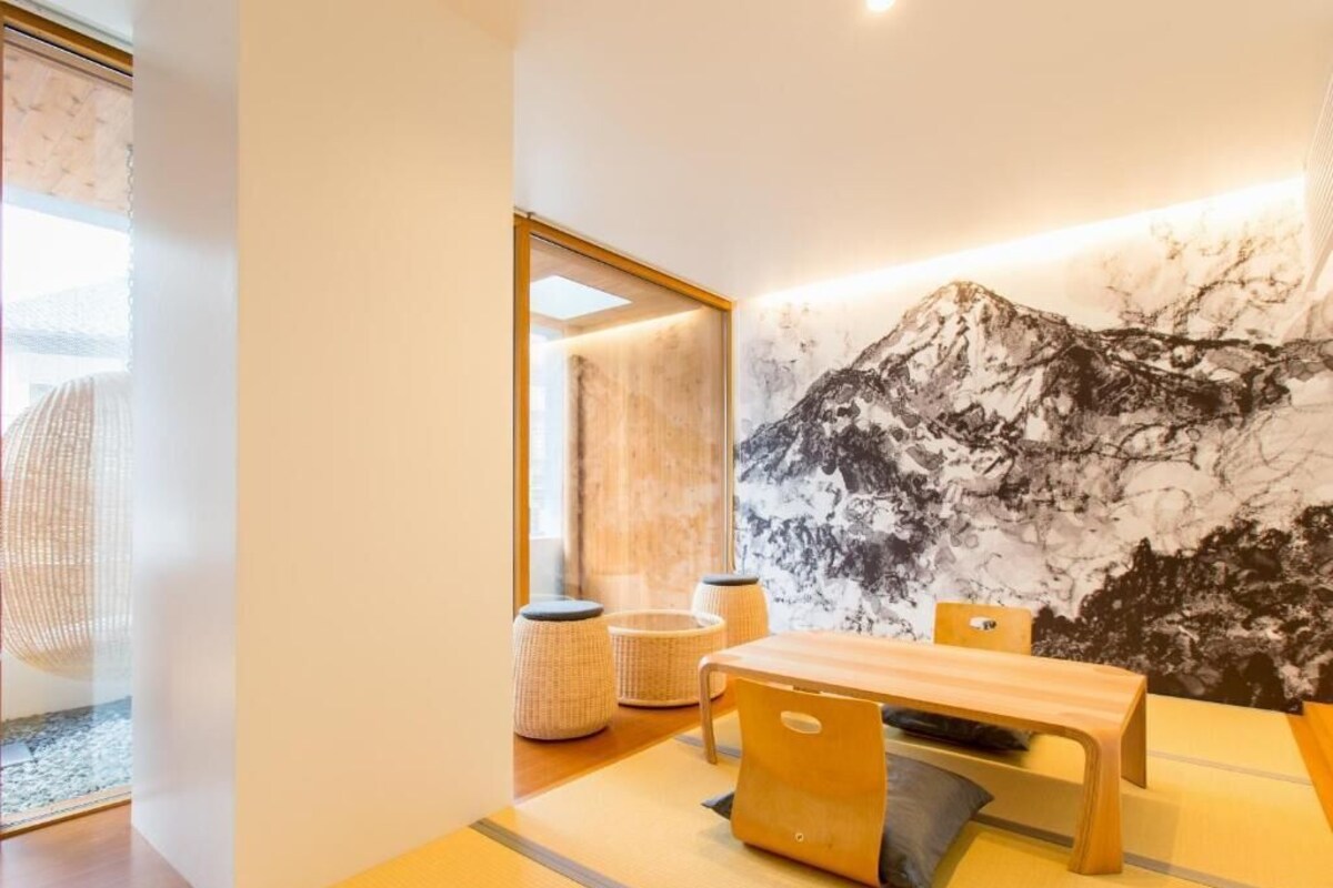Quarto moderno com mesa de madeira, cadeiras e um grande mural na parede com montanhas.