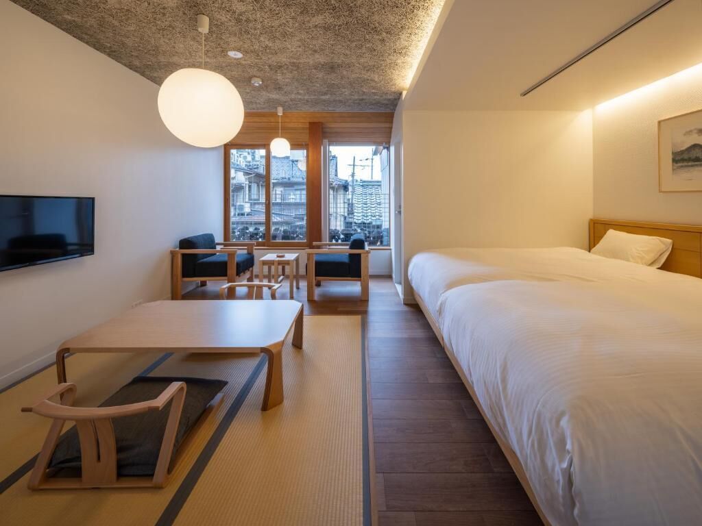 A hotel room with a bed, a desk, a chair, a television, and a view of the city.