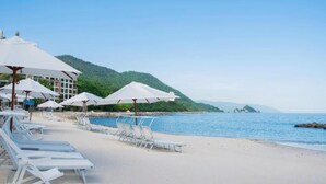 A beach with white lounge chairs and umbrellas, a building in the background, and a clear view of the sea and hills. - 2-Bedroom Suite at Garza Blanca, Puerto Vallarta (Puerto Vallarta)