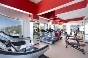 Ein Fitnessstudio mit Laufbändern, Trainingsgeräten und großen Fenstern mit Blick ins Freie.