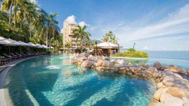 A resort pool with clear water, surrounded by palm trees and a building with a dome roof. - 2-Bedroom Suite at Garza Blanca, Puerto Vallarta (Puerto Vallarta)