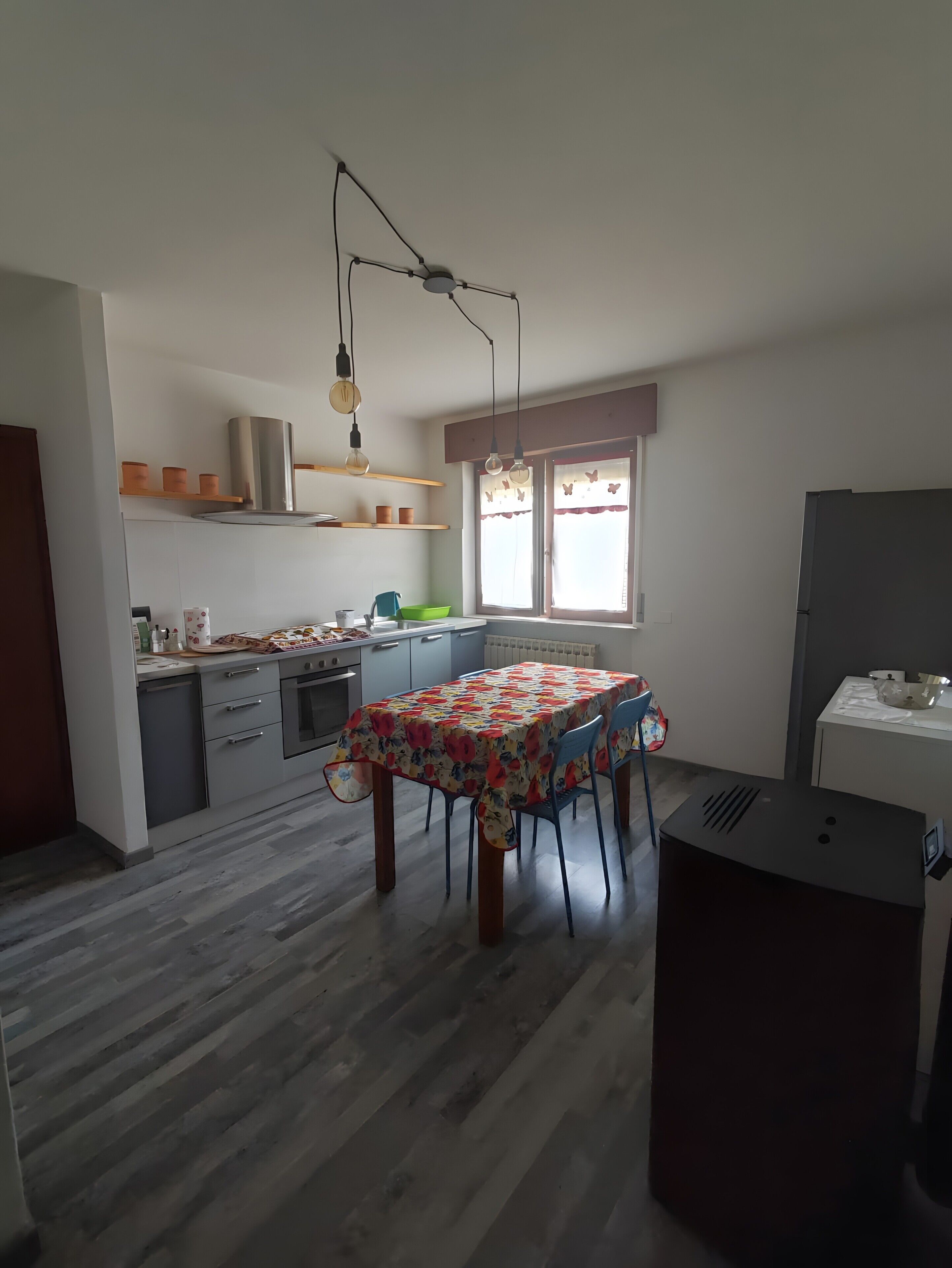 Une cuisine équipée d’une table à manger, de placards, d’un réfrigérateur et d’une fenêtre avec des rideaux.