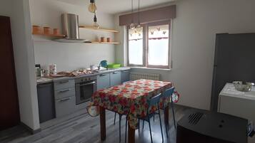Une cuisine équipée d’une table à manger, de placards, d’un réfrigérateur et d’une fenêtre avec des rideaux.