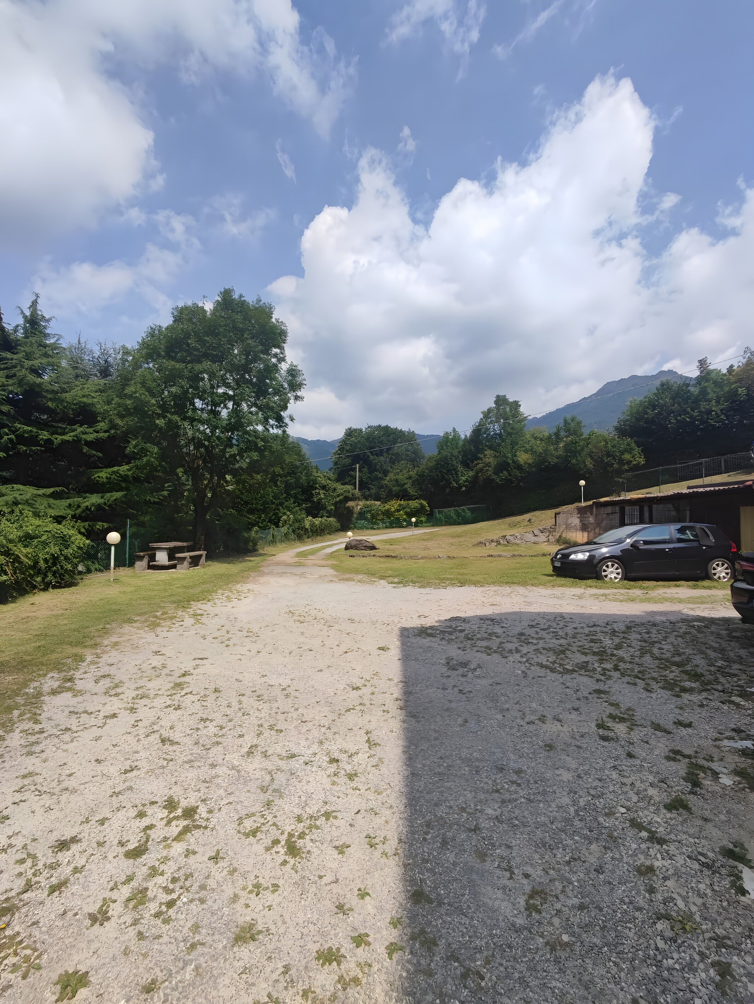 A gravel path leading to a picnic area with a bench, surrounded by greenery and a mountain in the background.