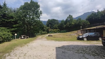 A gravel path leading to a picnic area with a bench, surrounded by greenery and a mountain in the background.