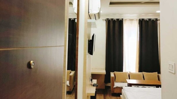 A hotel room with a wooden wardrobe, a desk with a chair, a bed, and a television mounted on the wall. - Hotel Silvora Inn - Bhopal (Bhopal)
