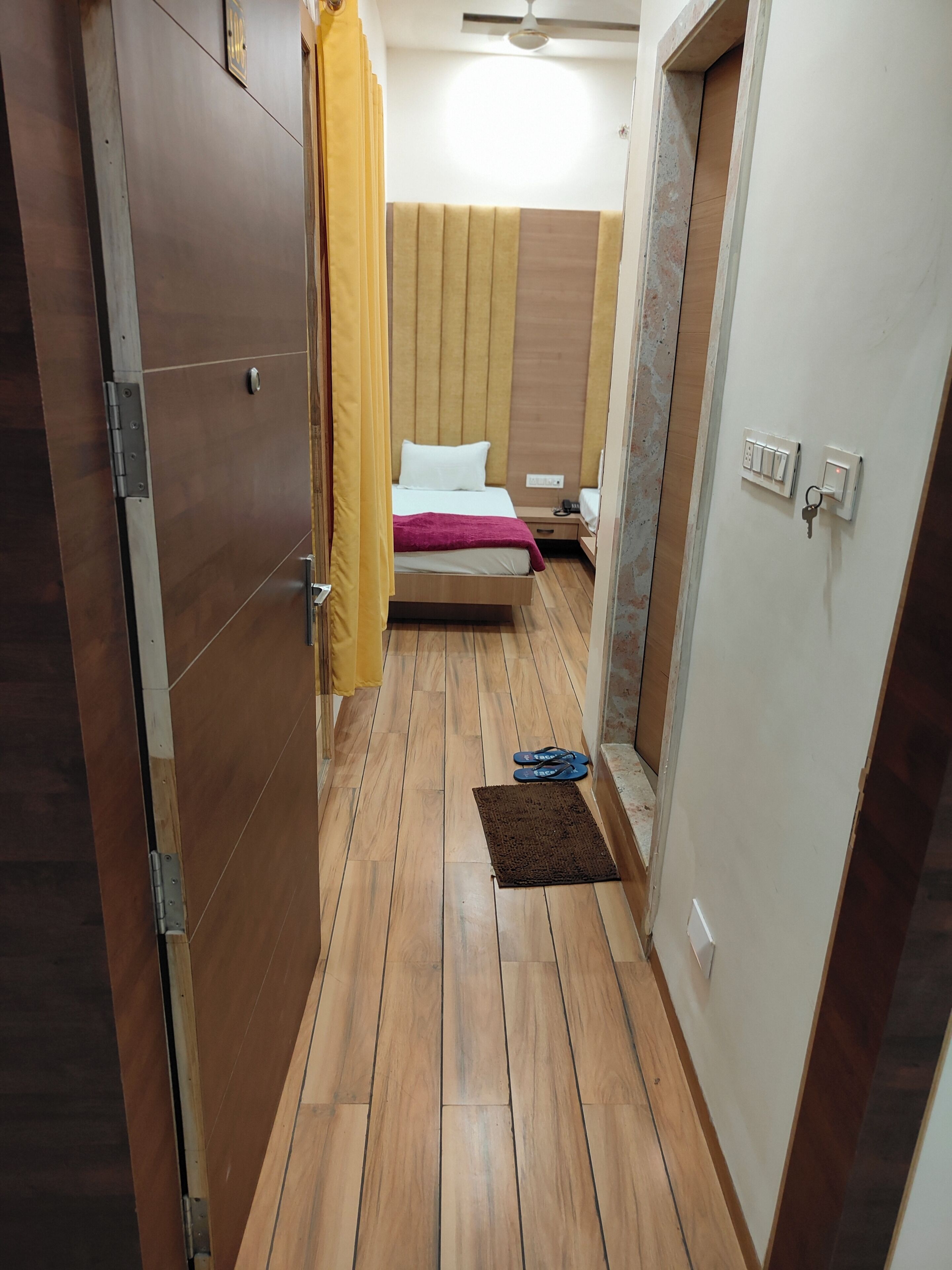 A narrow hallway with a bed, a door, and a light switch.