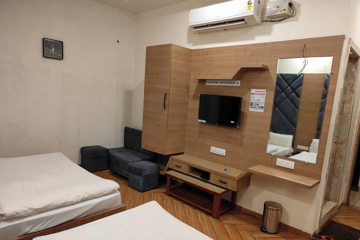 Habitación de hotel con dos camas, televisión, armario, espejo y un pequeño cubo de basura.