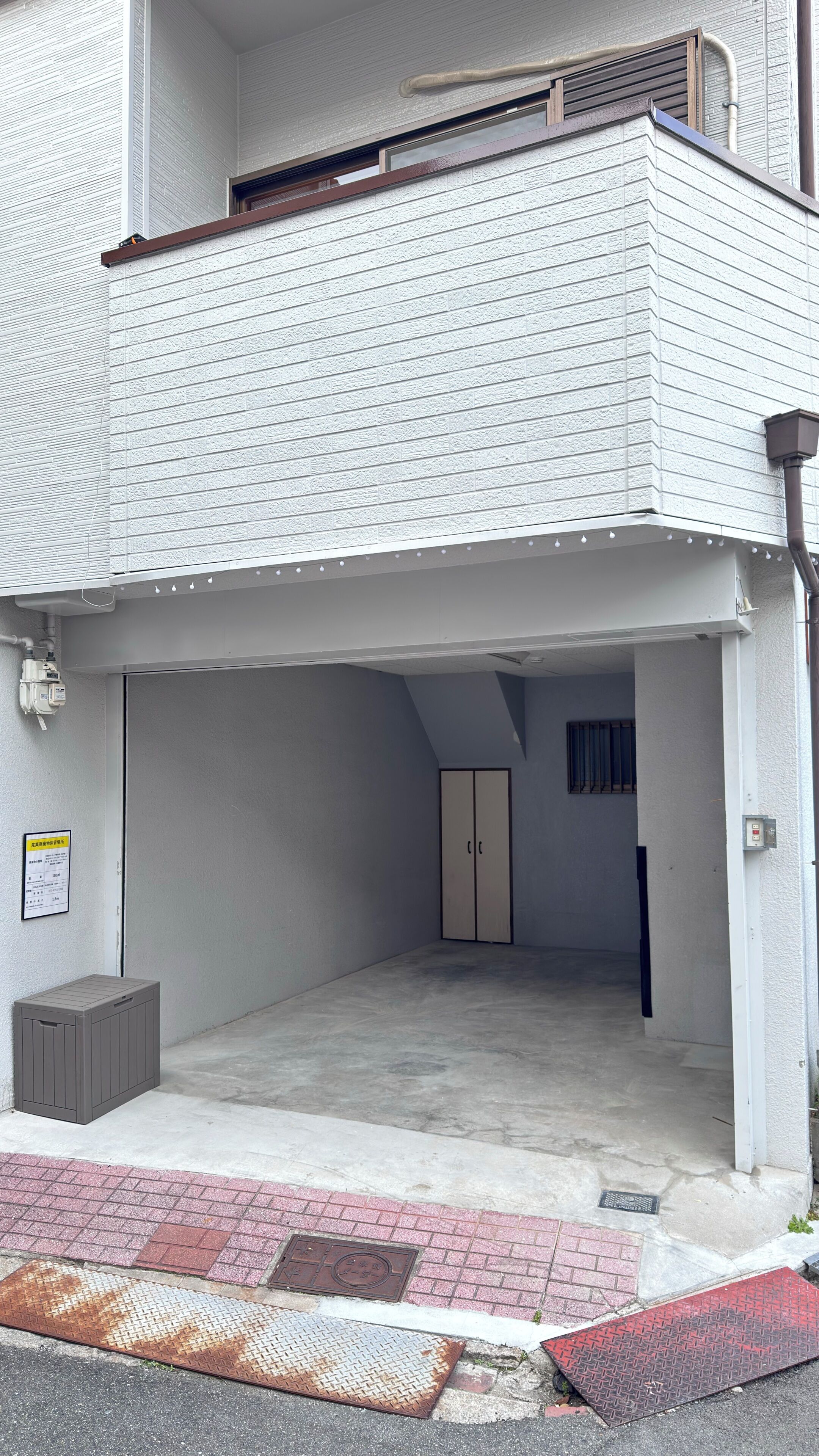 A building with a garage entrance, a small storage unit, and a metal grate on the ground.