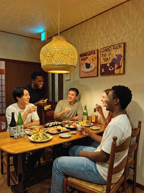 A group of people dining at a wooden table with various dishes, bottles, and a decorative hanging light fixture. - Funyado (Osaka)