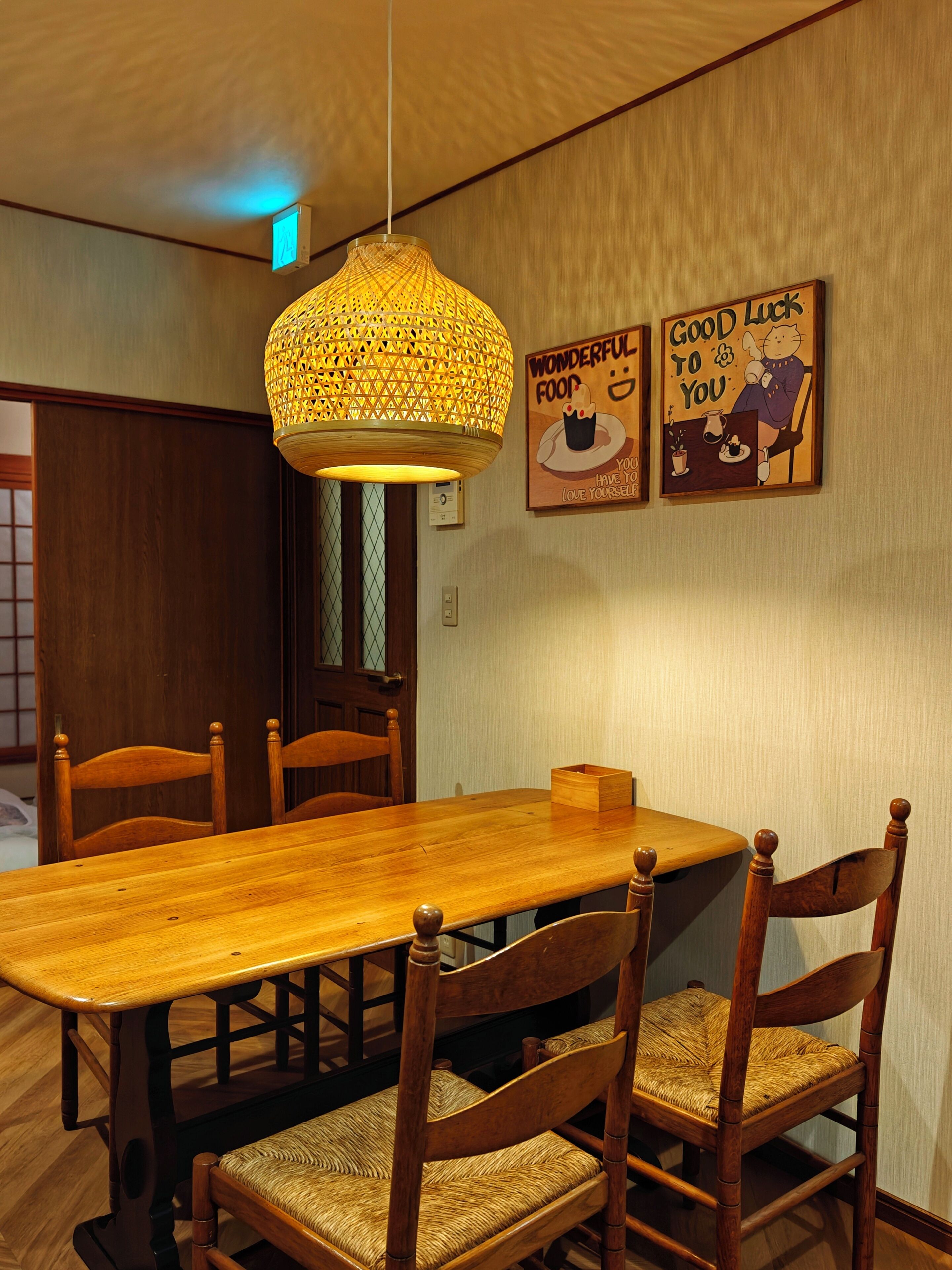 A dining area with a wooden table and chairs, a hanging light fixture, and two wall-mounted posters.