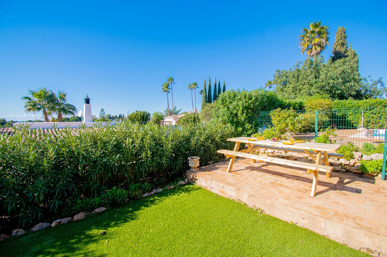 A patio area with a picnic table, lush greenery, and a clear blue sky.