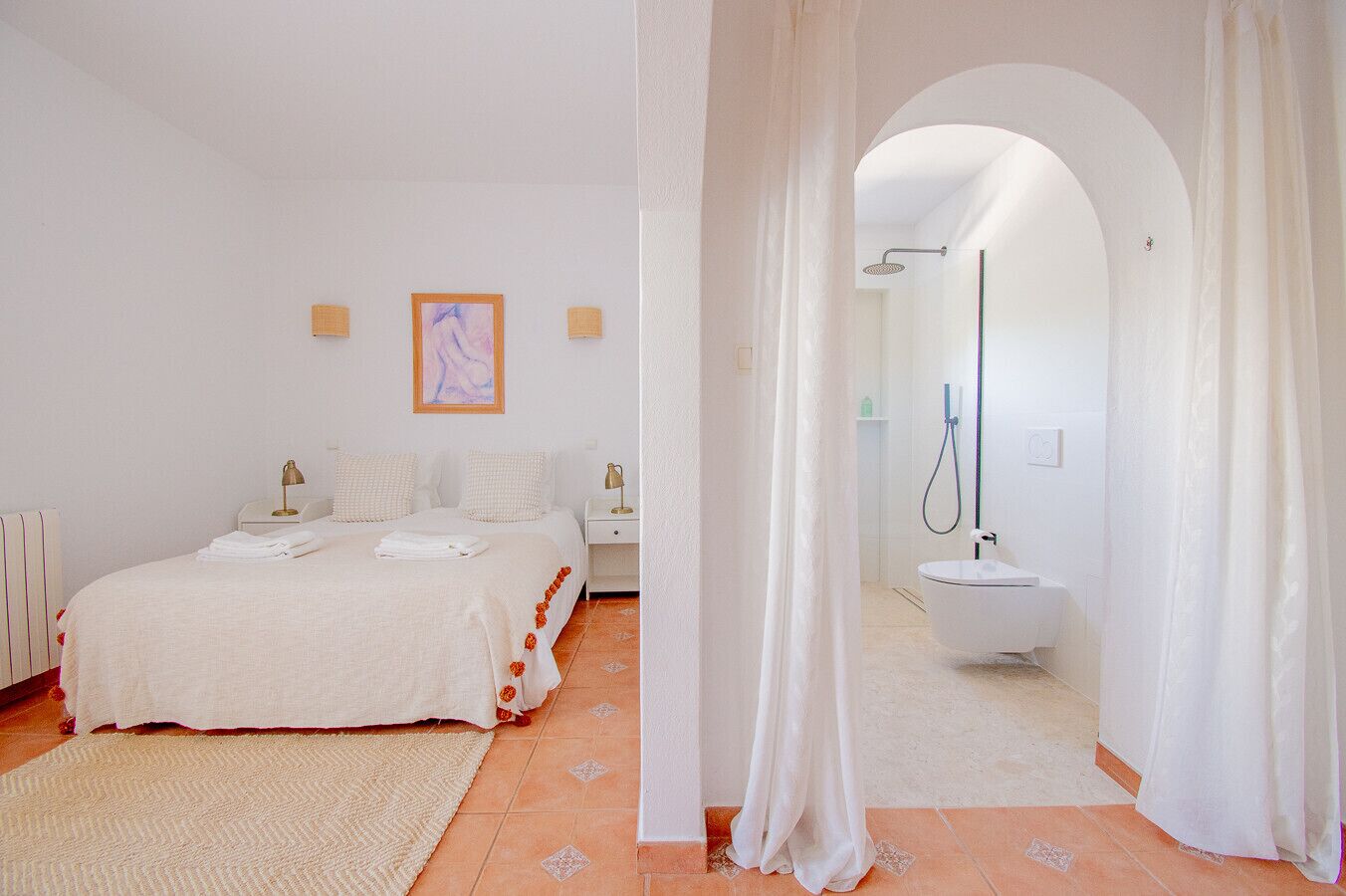 Un dormitorio con una cama, mesitas de noche y un cuadro. Incluye un baño con ducha, lavabo e inodoro.