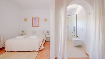 Un dormitorio con una cama, mesitas de noche y un cuadro. Incluye un baño con ducha, lavabo e inodoro.