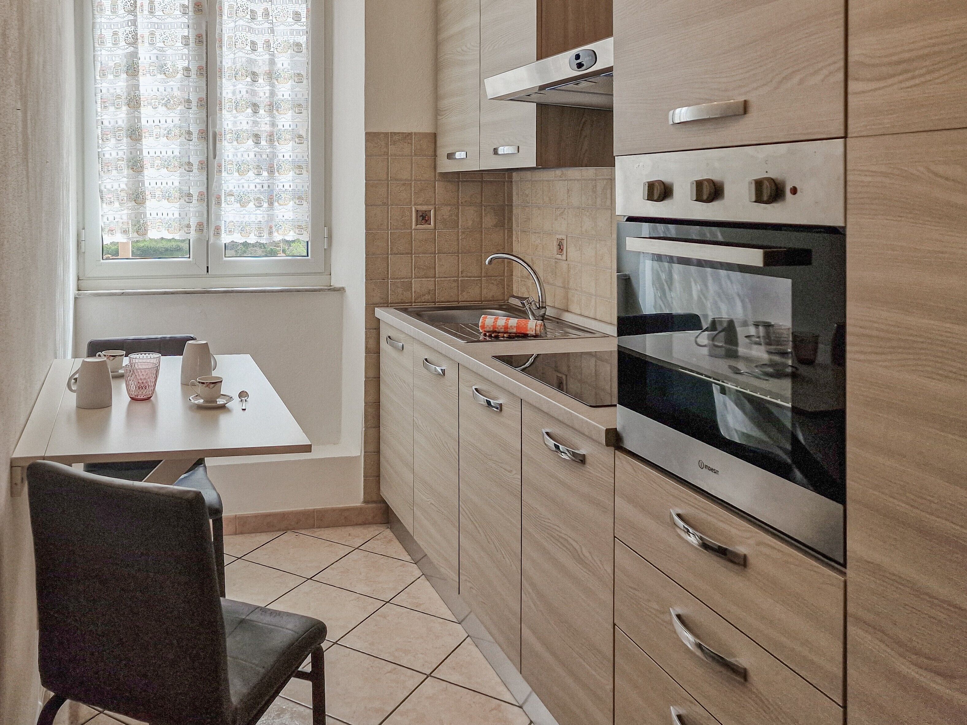 A compact kitchen with a window, a sink, a stove, and a dining area with chairs.
