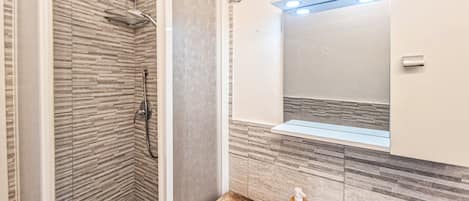 A bathroom with a shower, a sink with a mirror, and a wooden countertop.
