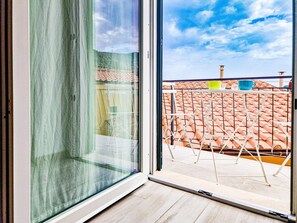 A room with a large window, a view of a tiled roof, and a metal railing outside. - Apartment 'Bilo Alex Rio Marina' (Rio Marina)