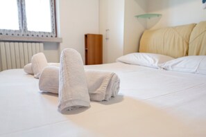 Una cama bien hecha con toallas blancas dobladas, una mesita de noche de madera y una lámpara de noche.