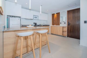 A modern kitchen with white cabinets, a wooden countertop, and two bar stools. - Corporate Stays First del Sol (Asunción)