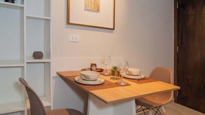 Een eetruimte met een tafel gedekt voor twee personen, stoelen, een ingelijste foto aan de muur en een witte wandplank.