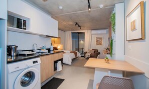 A compact hotel room with a kitchenette, a washing machine, a dining area, a sofa, and a TV. - Corporate Stays First del Sol (Asunción)
