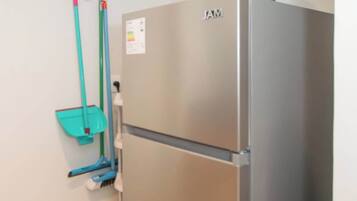 A stainless steel refrigerator with a black appliance on top, a wall-mounted mop rack, and a broom leaning against the wall.