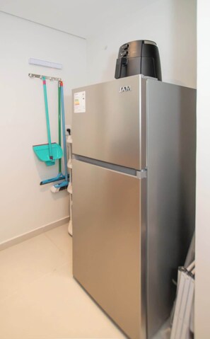 Un refrigerador de acero inoxidable con un electrodoméstico negro encima, un porta escoba en la pared y una escoba apoyada contra la pared.