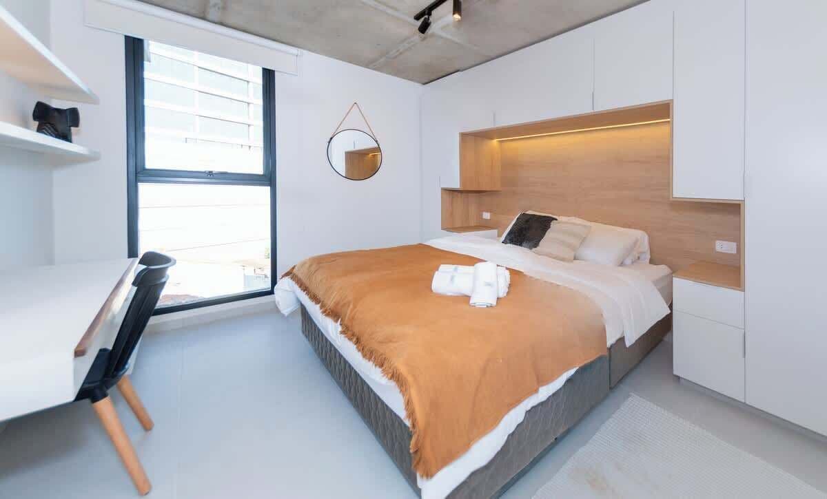 Un dormitorio moderno con una cama, un escritorio y una ventana.