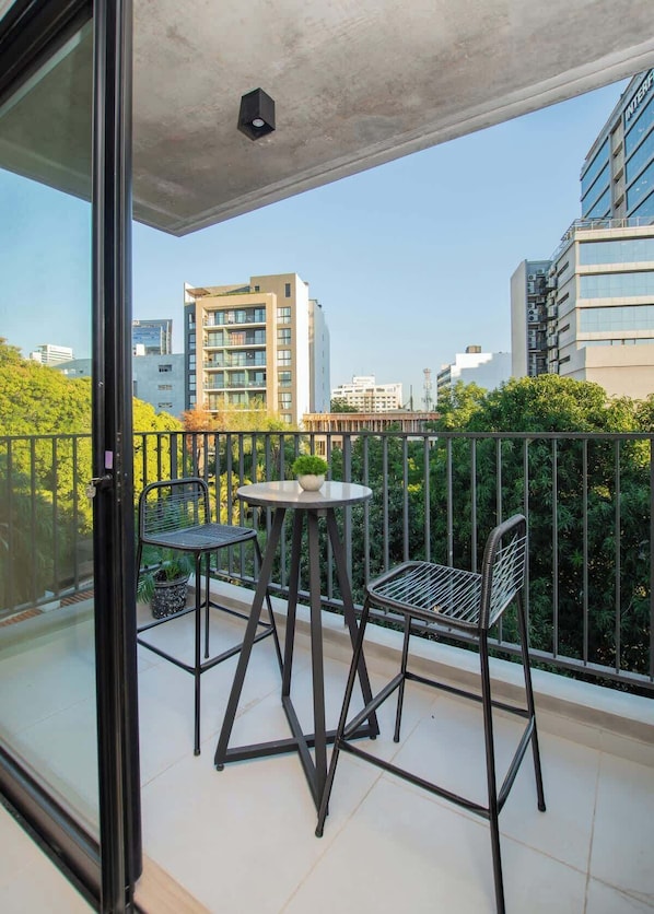 Ein Balkon mit zwei Stühlen und einem kleinen Tisch, mit Blick auf eine Stadtlandschaft mit modernen Gebäuden.