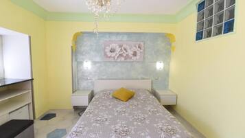 Un dormitorio con cama, mesitas de noche, candelabro, un cuadro y una ventana con persianas.