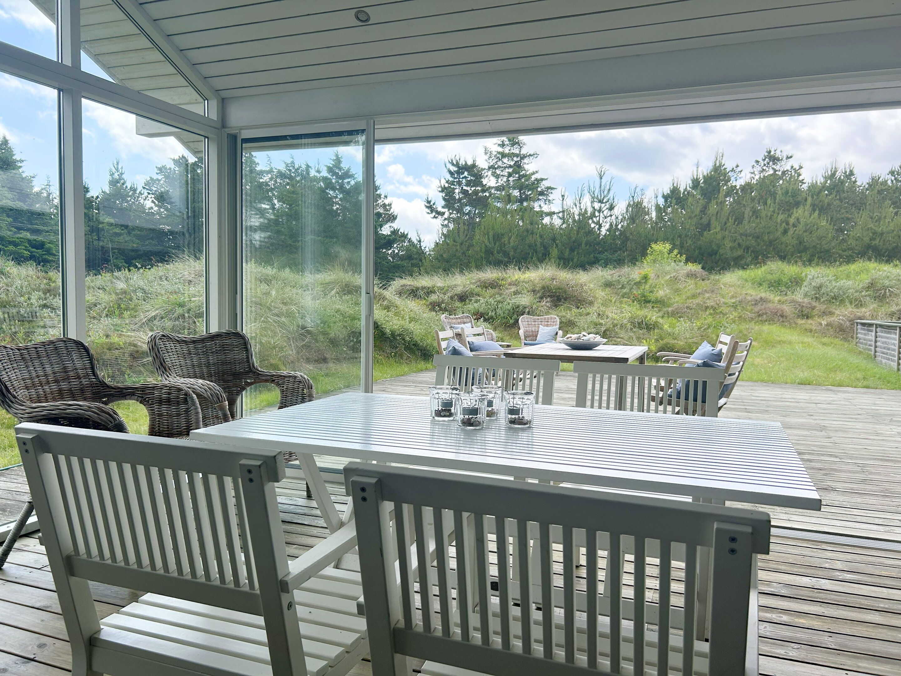 A covered outdoor deck with a table and chairs, overlooking a grassy area with trees.