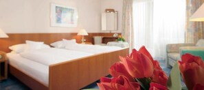 A hotel room with a large bed, a nightstand, a lamp, and a window with curtains. - NaturMed Hotel am Park (Badenweiler)