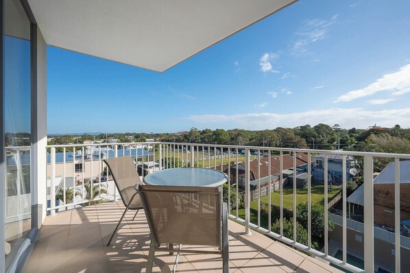 A balcony with a table and chairs, offering a view of a residential area and a distant landscape. - Resort Studio Steps to Beach & Pool (Caloundra)
