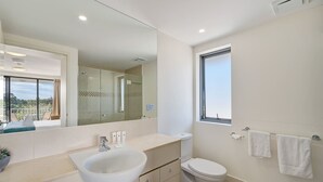 A modern bathroom with a large mirror, a sink, a toilet, and a window. - Resort Studio Steps to Beach & Pool (Caloundra)