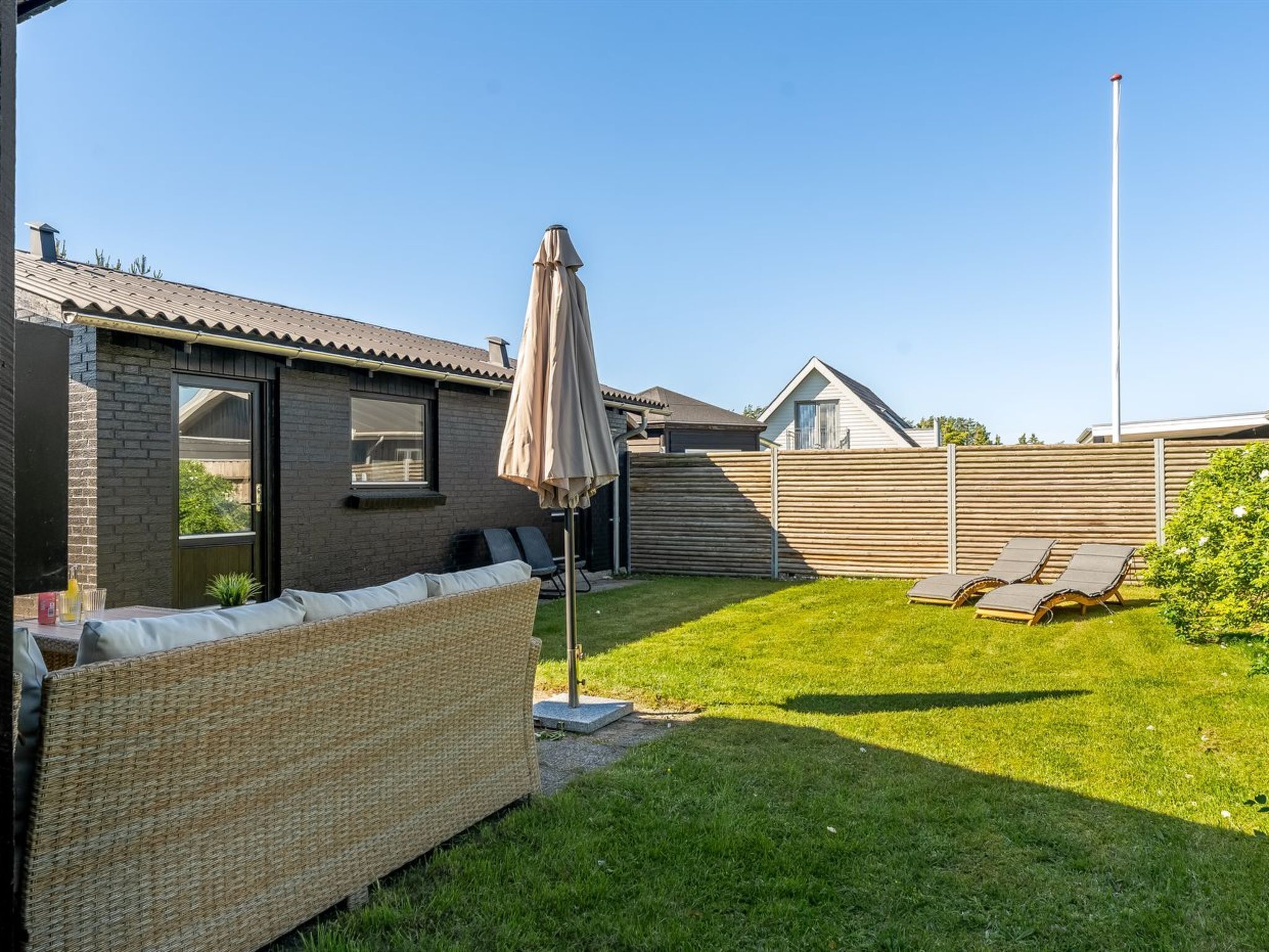 Ein Garten mit einem Korbsessel, Sonnenschirm und Rasen mit Liegestühlen.