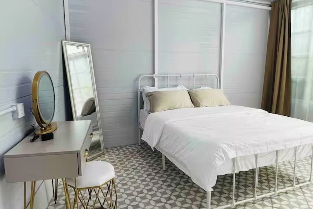A bedroom with a bed, a bedside table, a mirror, and a window with curtains.