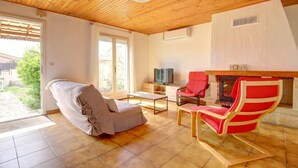 A room with a wooden ceiling, a sofa, a red chair, a television, and a fireplace. - The Van Gogh House: 3 bedrooms, 4 beds, and easy parking (Tournefeuille)