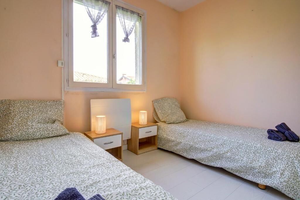 A bedroom with two beds, a window with curtains, bedside lamps, and a small table.